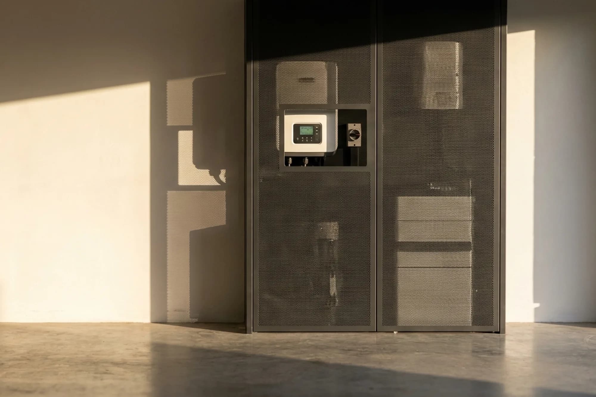 Ventilated laser-cut aluminium screen covering a wall-mounted solar inverter and battery bank