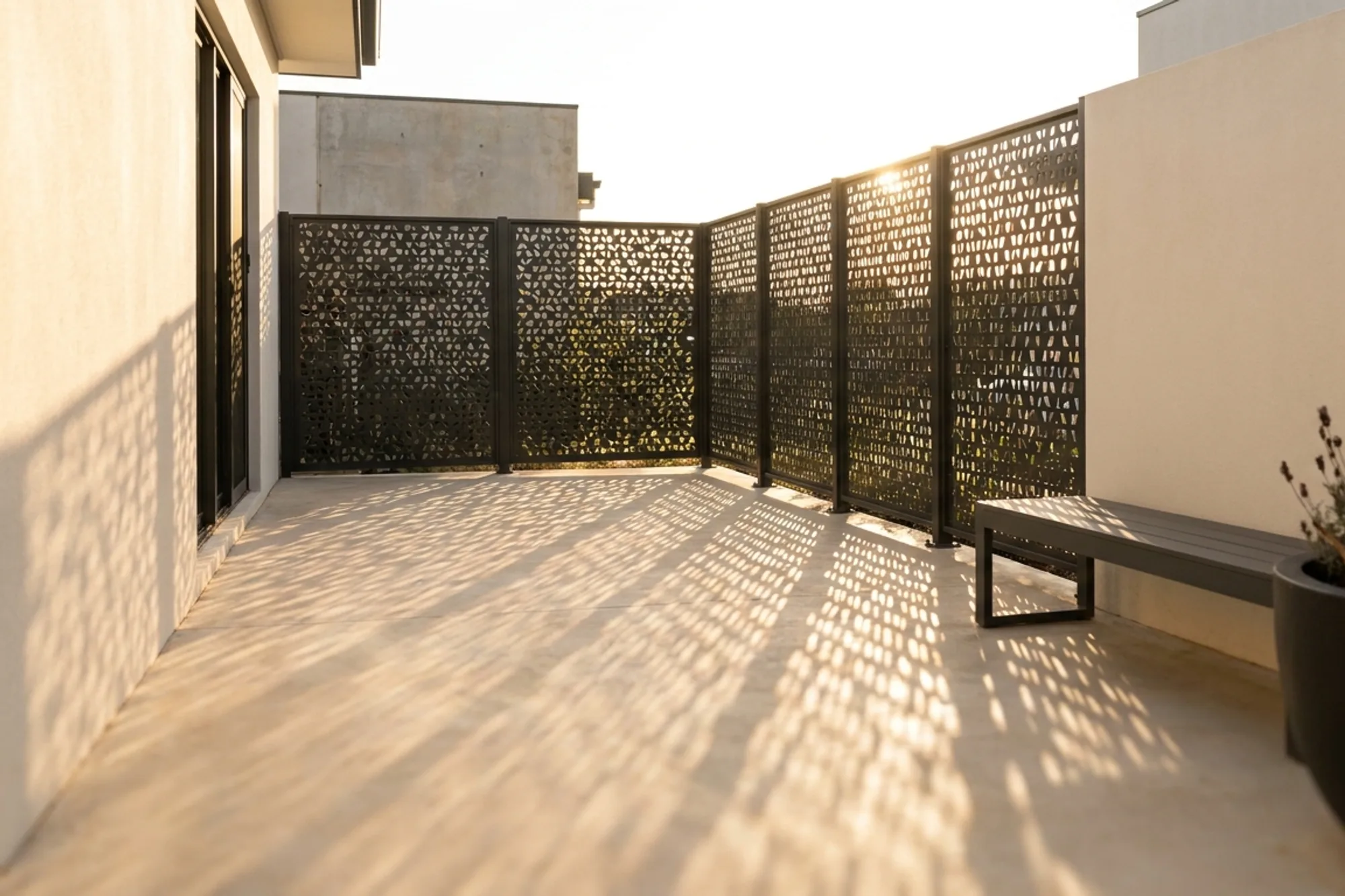 Tall laser-cut aluminium privacy screen dividing a residential courtyard in late sun